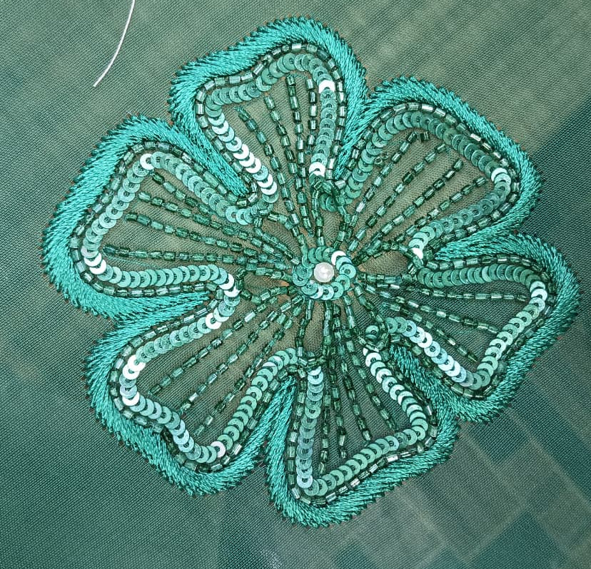 Teal embroidered flower design on a green fabric background