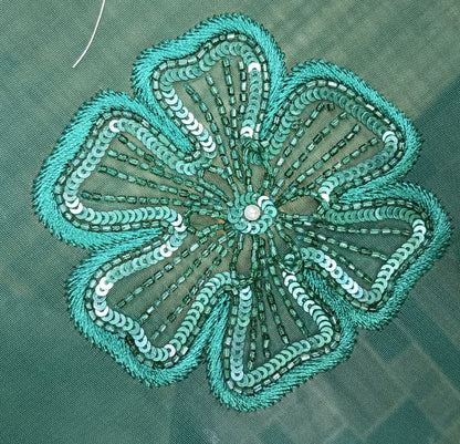 Teal embroidered flower design on a green fabric background